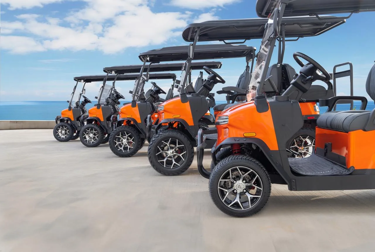 Flota de carros de golf eléctricos Denago naranja en resort frente al mar